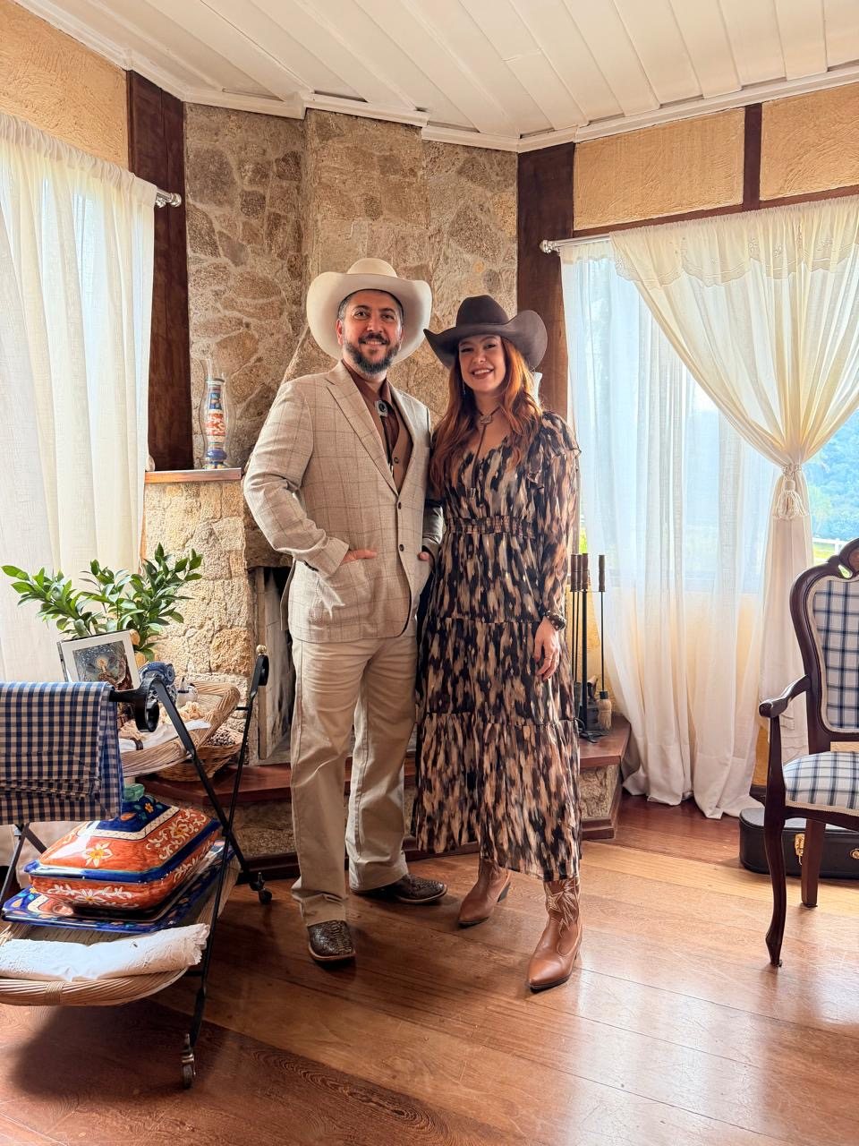 Bruno e Sofia Gayoso de chapéu, terno claro, vestido e botas numa sede de fazenda