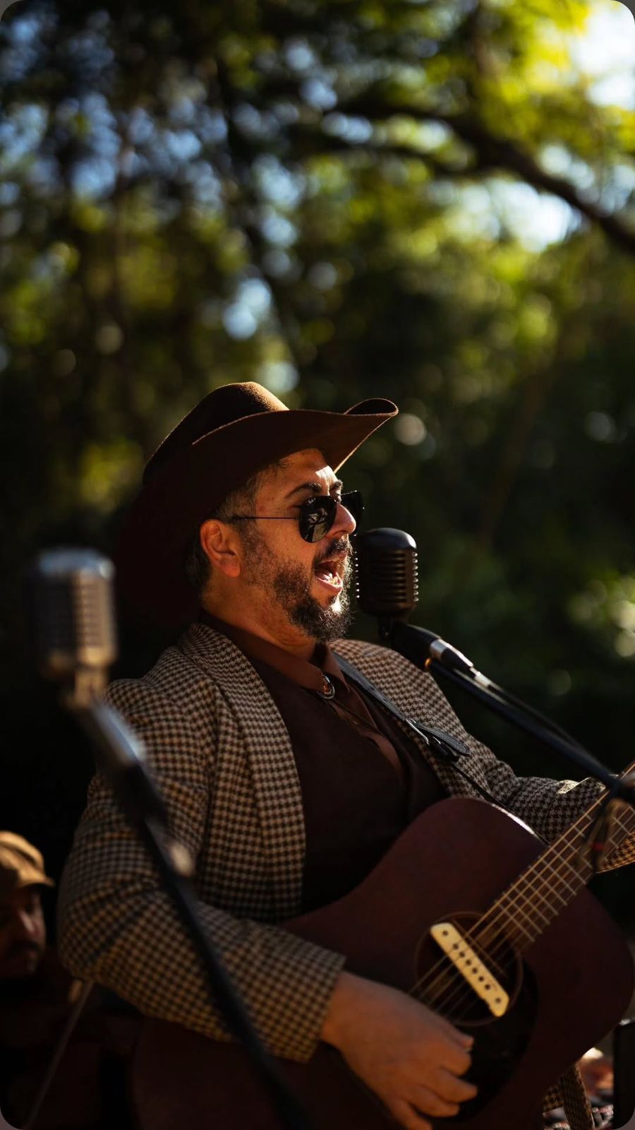 Cantor de chapéu e óculos tocando violão no jardim
