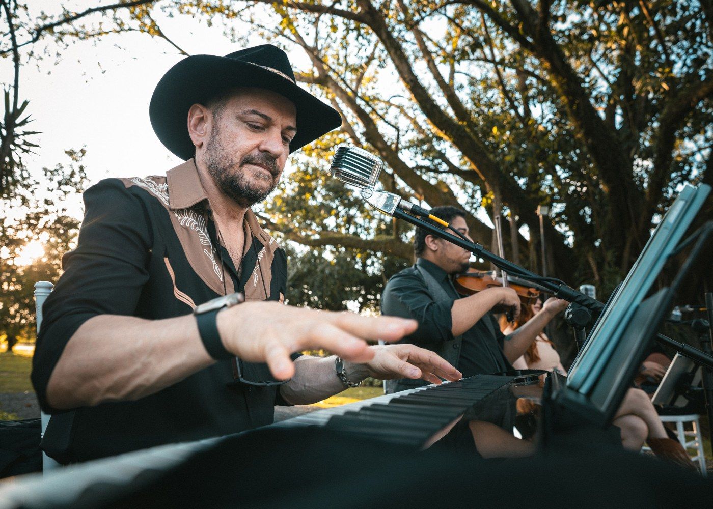 Pianista de chapéu tocando teclado com o violinista ao lado na cerimônia
